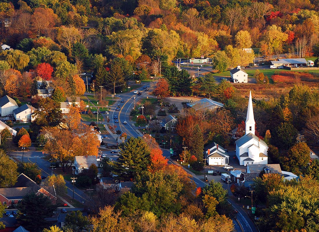 About Our Agency - Aerial View of a Small Massachusetts Town with a Curved Road and Homes and Businesses Surrounded by Colorful Fall Foliage