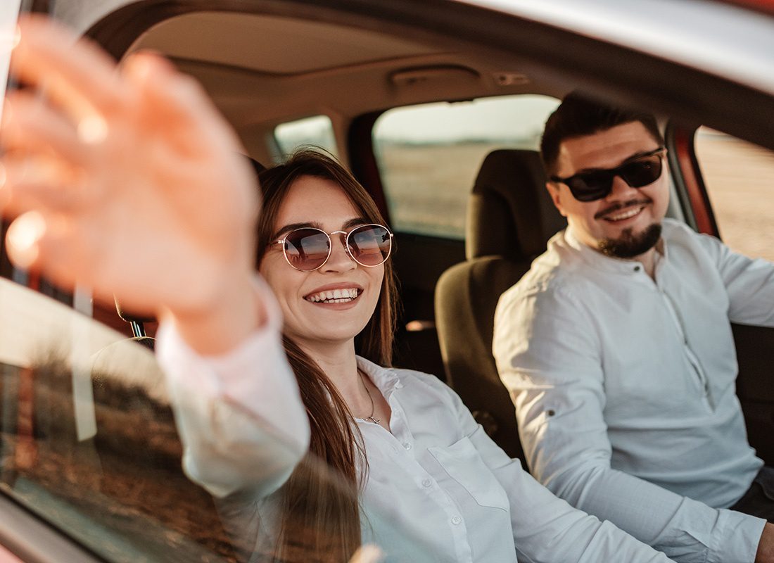 Insurance Solutions - Portrait of a Cheerful Young Couple Wearing Sunglasses Traveling in a Car on a Summer Road Trip