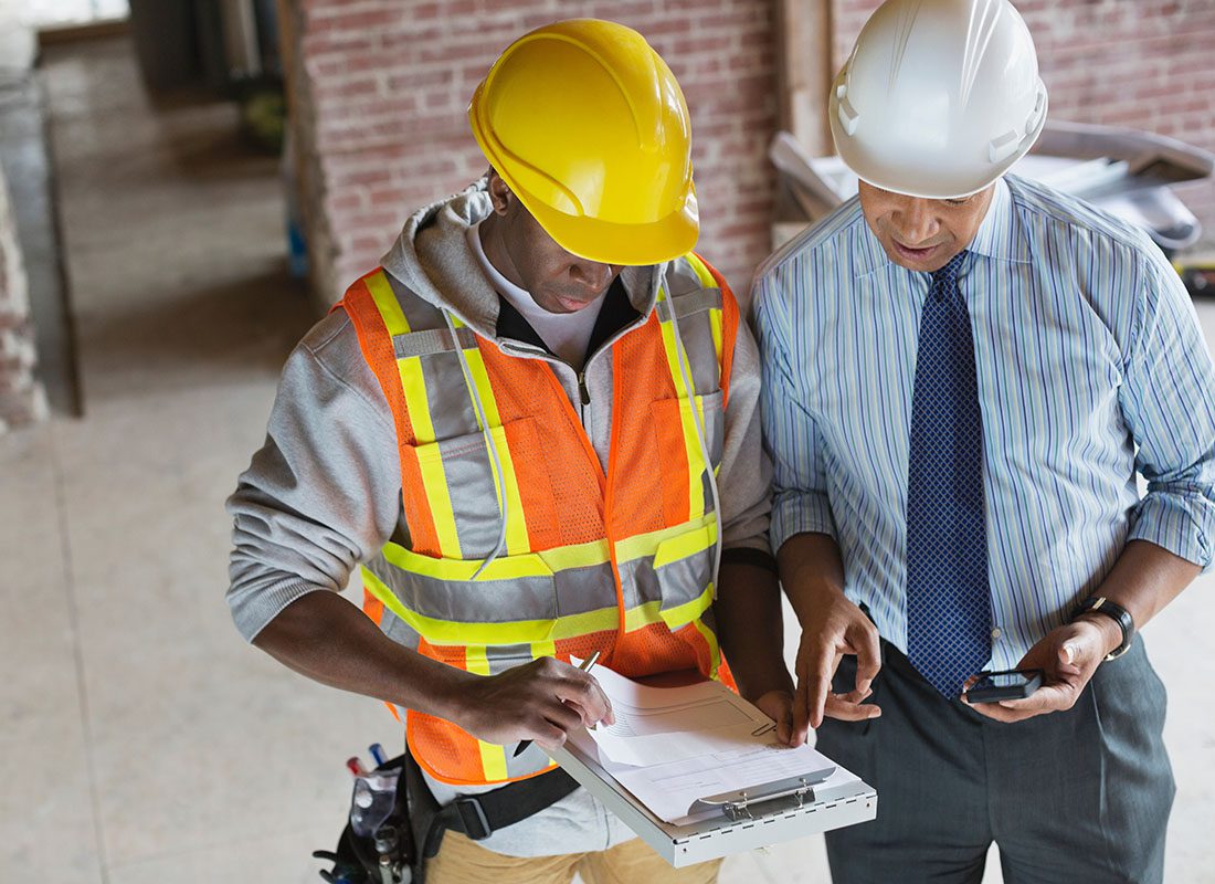 Insurance by Industry - Portrait of a Male Contractor and Engineer Looking at and Discussing Paperwork While They Both Stand in a New Building Construction Project